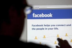 Bath, United Kingdom - May 4, 2011: Close-up of the Facebook homepage displayed on a LCD computer screen with silhouette of a man's head and hand out of focus in the foreground.